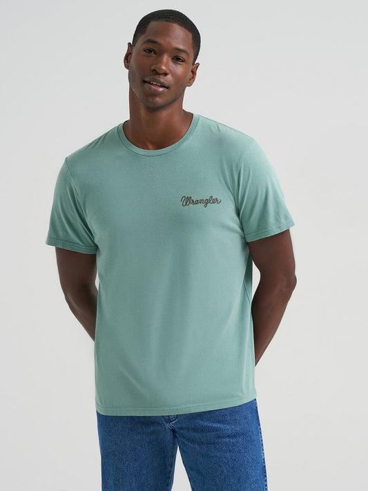Man wearing a light green t-shirt with a brand logo on a plain background