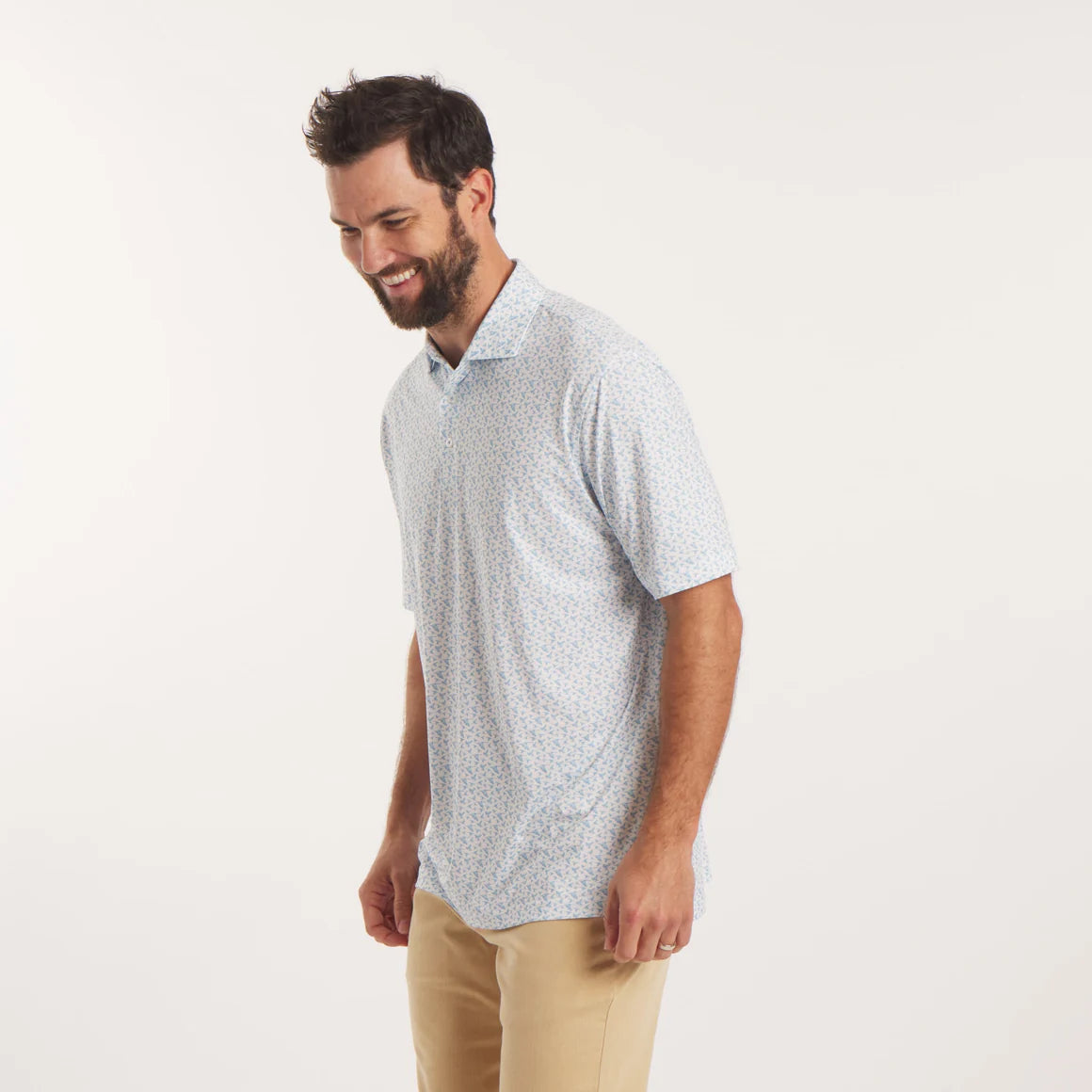 Man wearing a light gray patterned polo shirt and beige pants on a white background