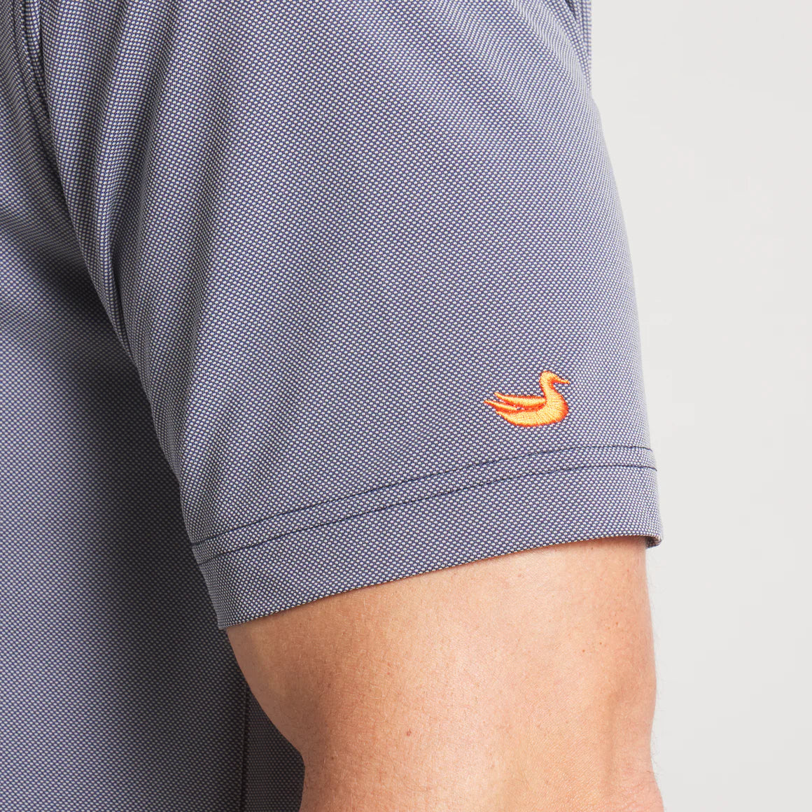 Close-up of gray short sleeve shirt with orange duck embroidery on sleeve.