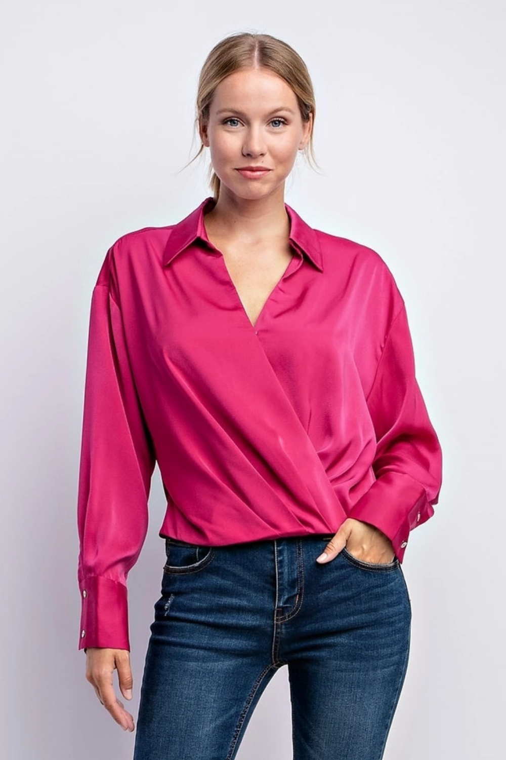 Woman wearing a stylish hot pink satin blouse and dark blue jeans against white background