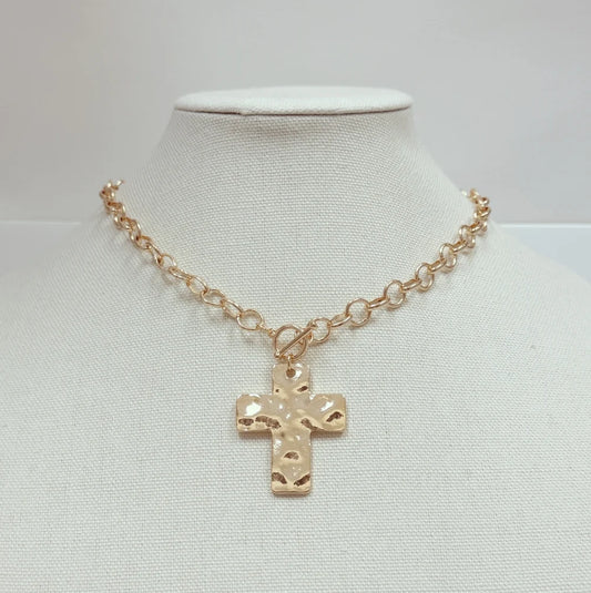 A gold-toned chain necklace with a textured cross pendant, displayed on a white fabric neck mannequin against a light gray background.