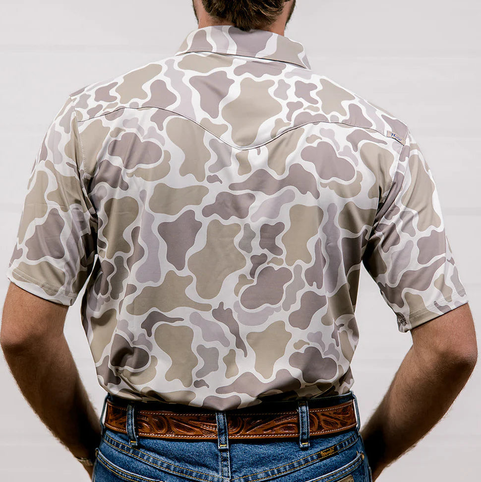 Person wearing a camouflage-patterned shirt and jeans on a plain background