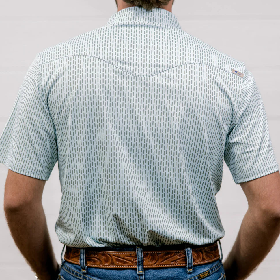 Person wearing a patterned shirt with a visible brand logo on a plain background