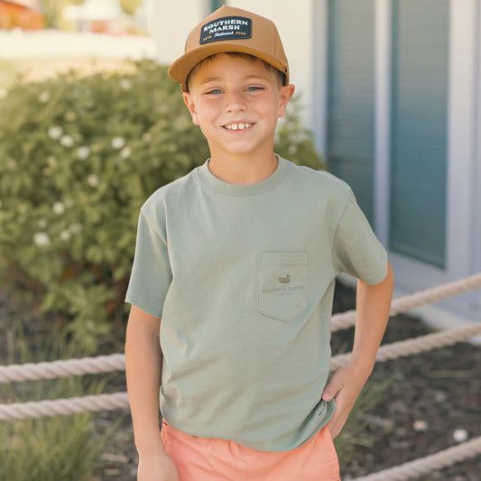 Young boy wearing a green t-shirt and brown cap with visible branding, standing outdoors.