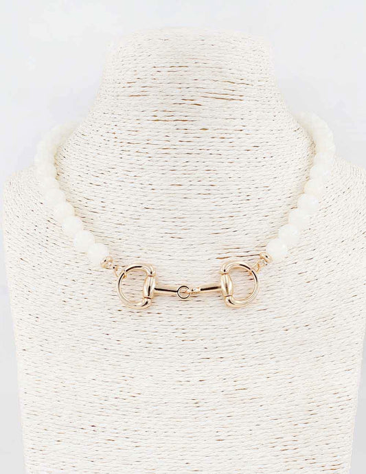 Gold horsebit necklace on a textured white stand