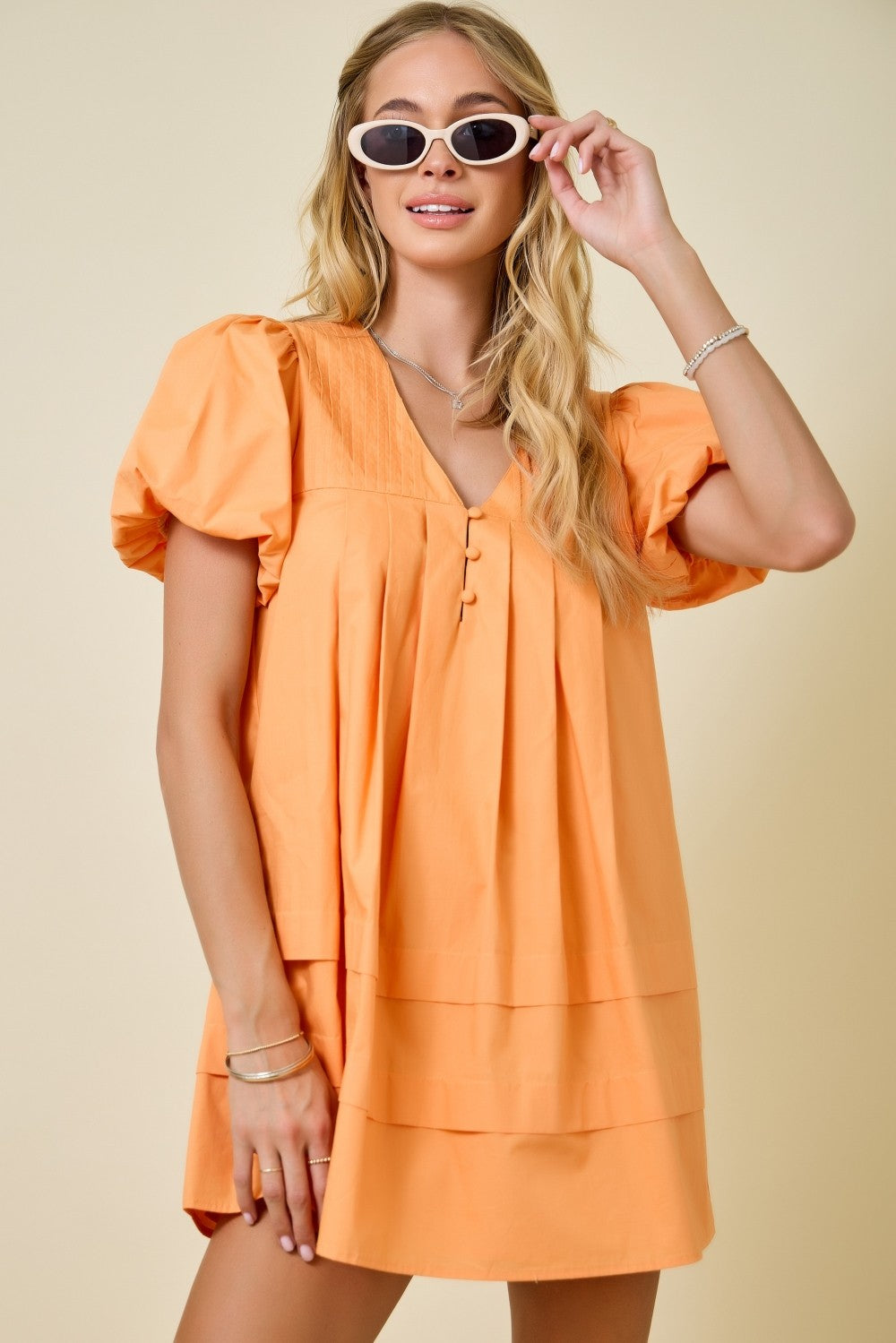 Woman wearing an orange dress and sunglasses on a beige background