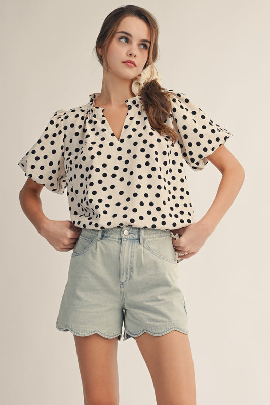 Woman wearing a polka dot blouse and denim shorts against a plain background