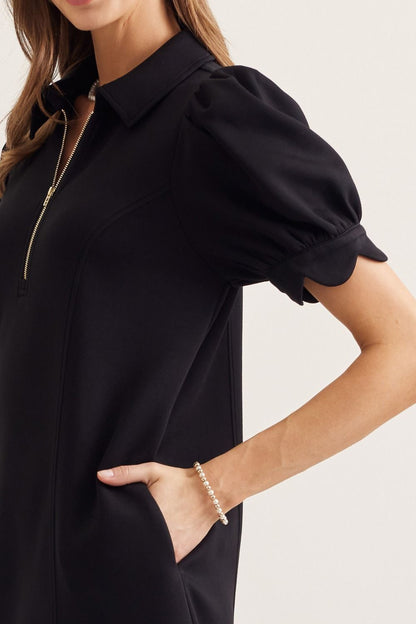 Person wearing a black dress with puffed sleeves on a neutral background