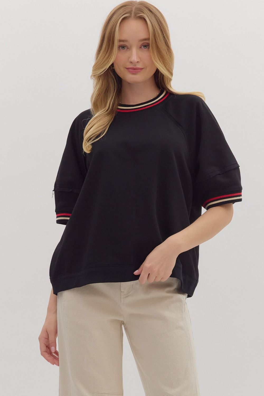 Woman wearing black short sleeve top with contrast striped collar and cuffs, beige pants