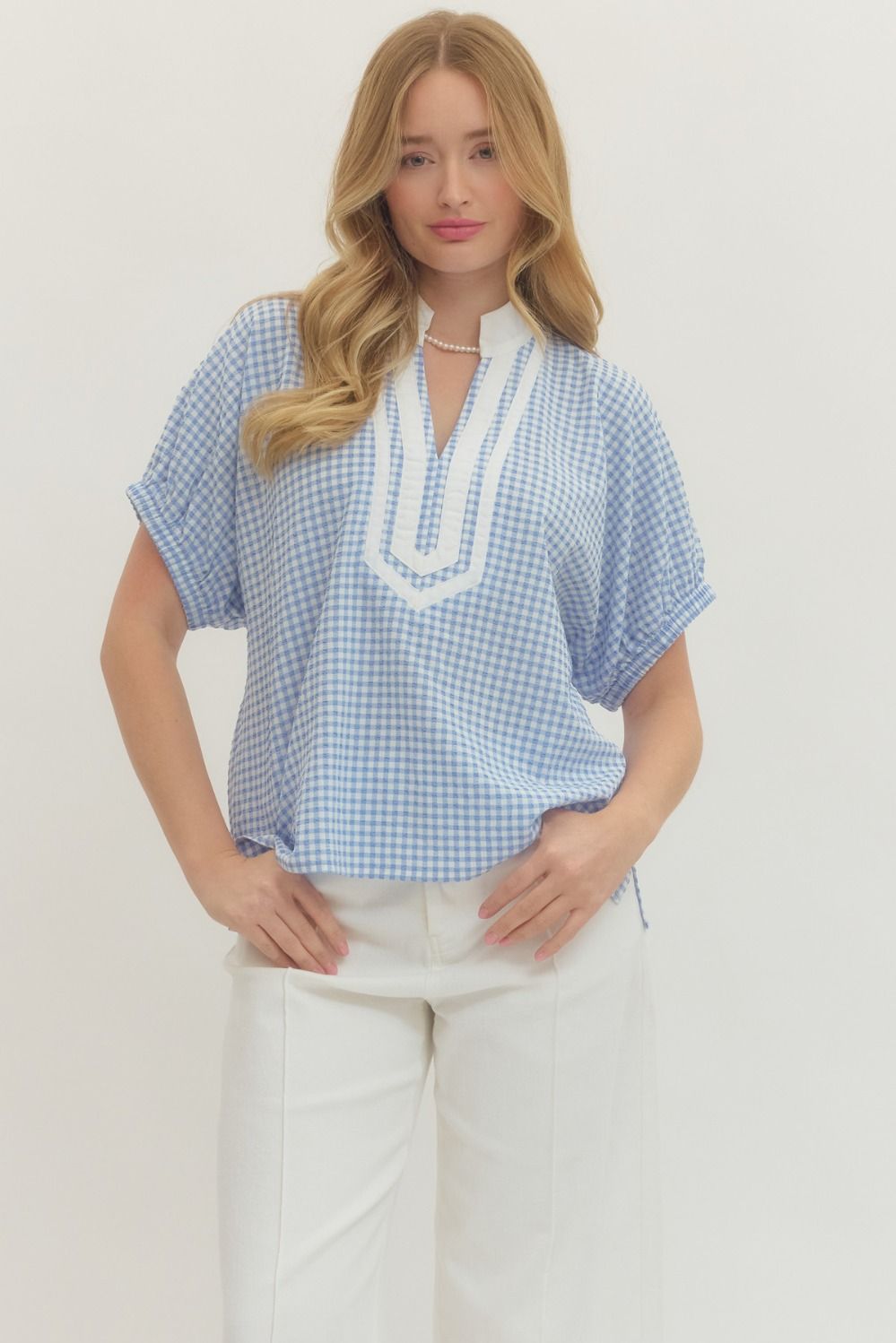 Woman wearing a blue checkered top with white trim on a plain background
