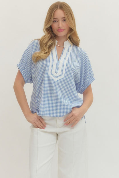 Woman wearing a blue checkered top with white trim on a plain background