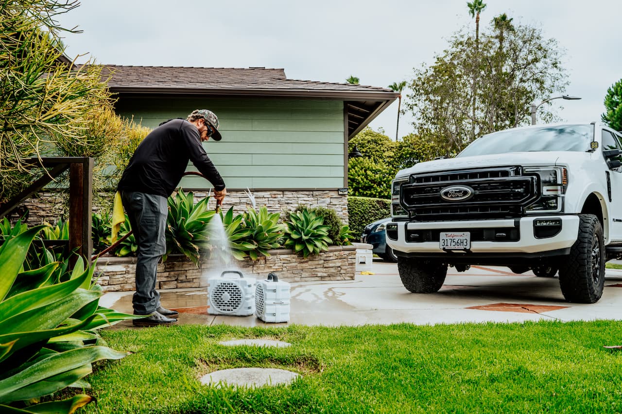 Person using a pressure washer next to a white Ford truck in a driveway.