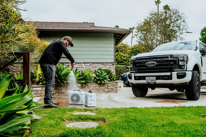 Person using a pressure washer next to a white Ford truck in a driveway.