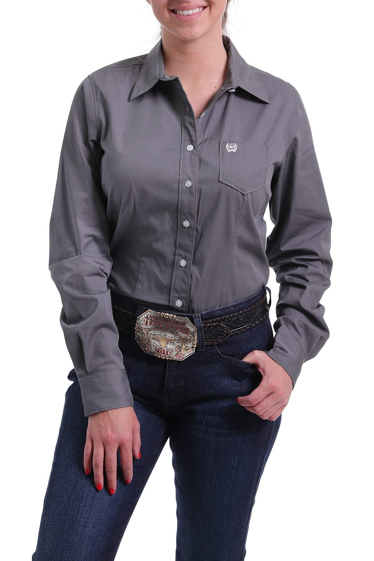 Woman wearing a gray western button-up shirt, dark jeans, and a large rodeo belt buckle