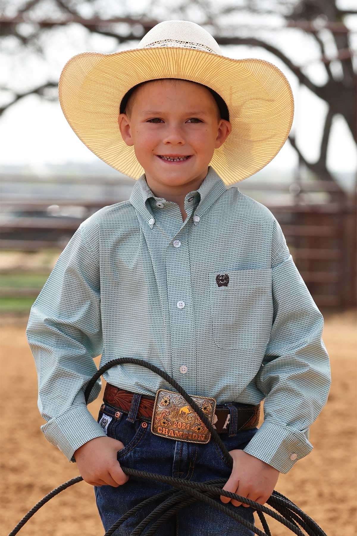 Young boy in cowboy attire holding a lasso outdoors.