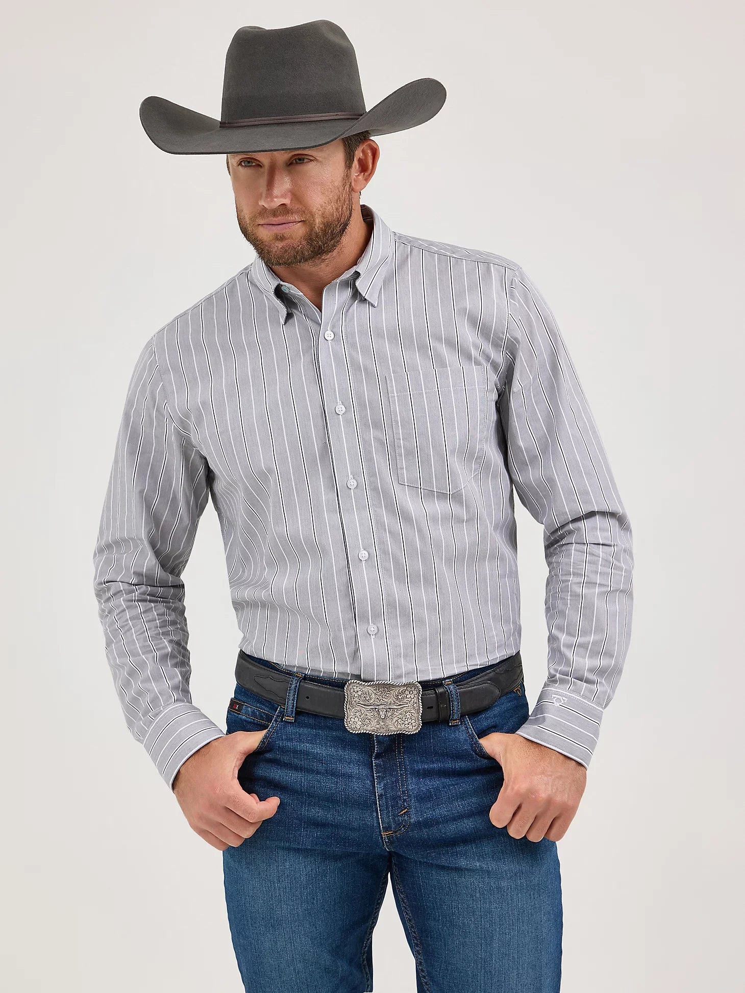 Man in gray striped western shirt, cowboy hat, blue jeans, and decorative silver belt buckle