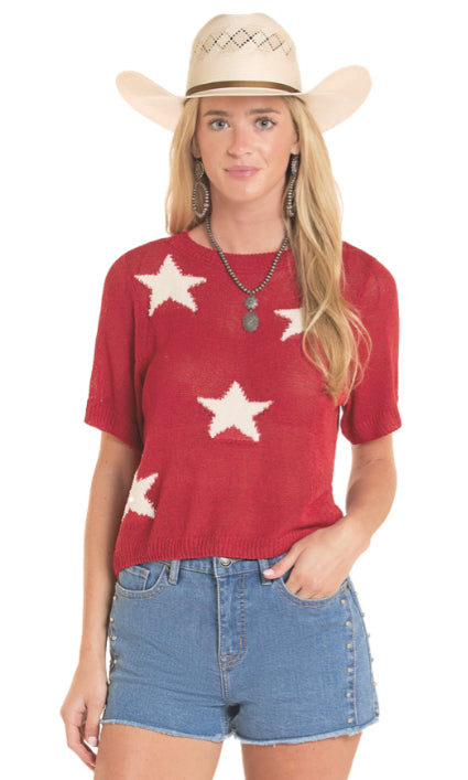 Woman wearing a red sweater with white star patterns, denim shorts, and a cowboy hat on a white background