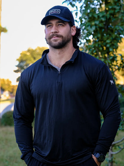 Man wearing a black jacket and cap with a logo, standing outdoors.