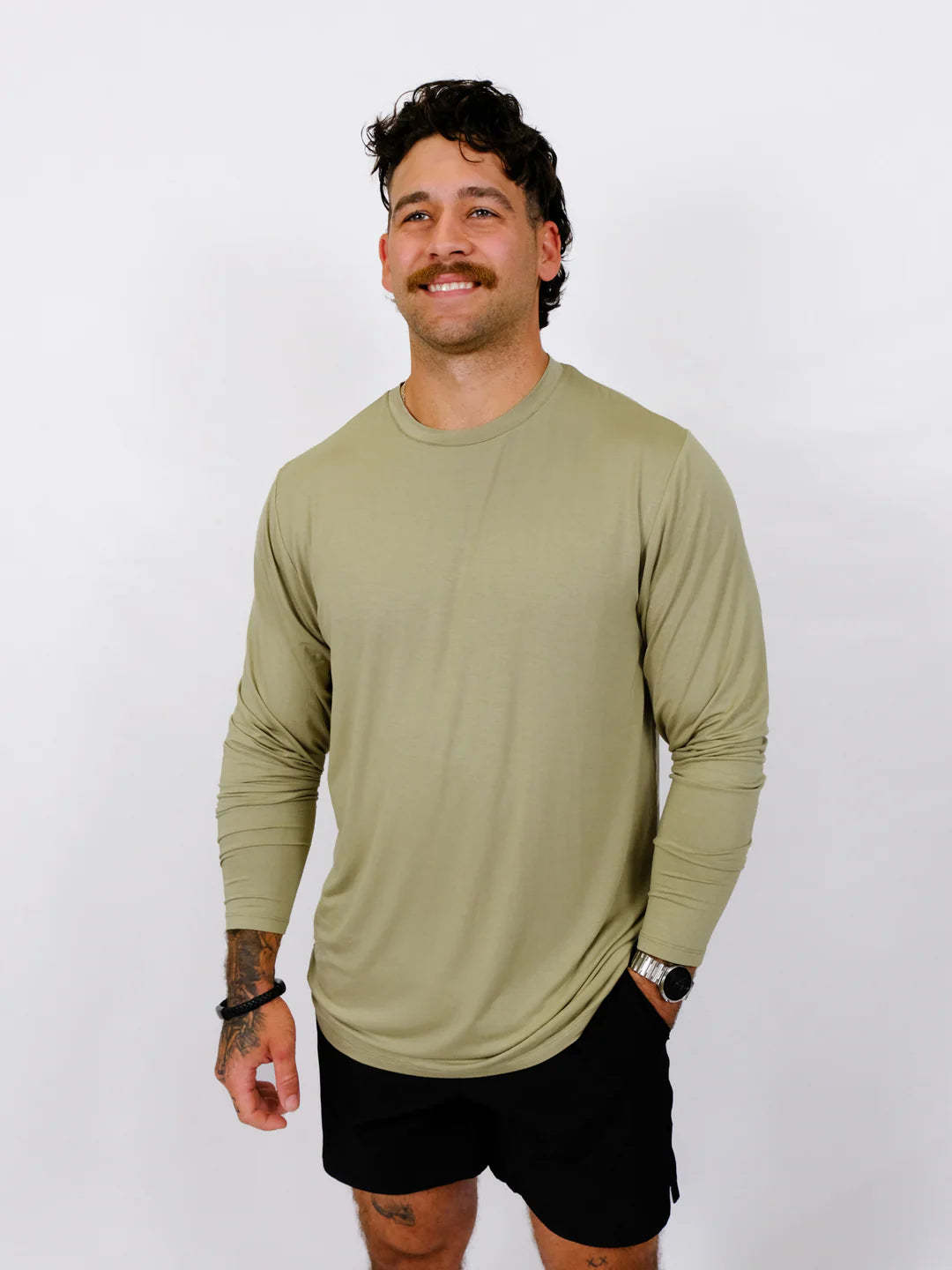 Man wearing a green long-sleeve shirt and black shorts against a white background