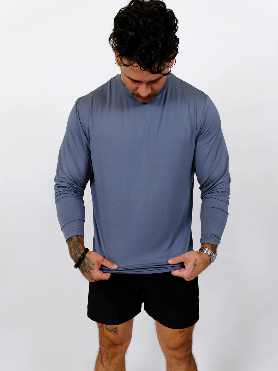 Man wearing a blue long-sleeve shirt and black shorts on a white background