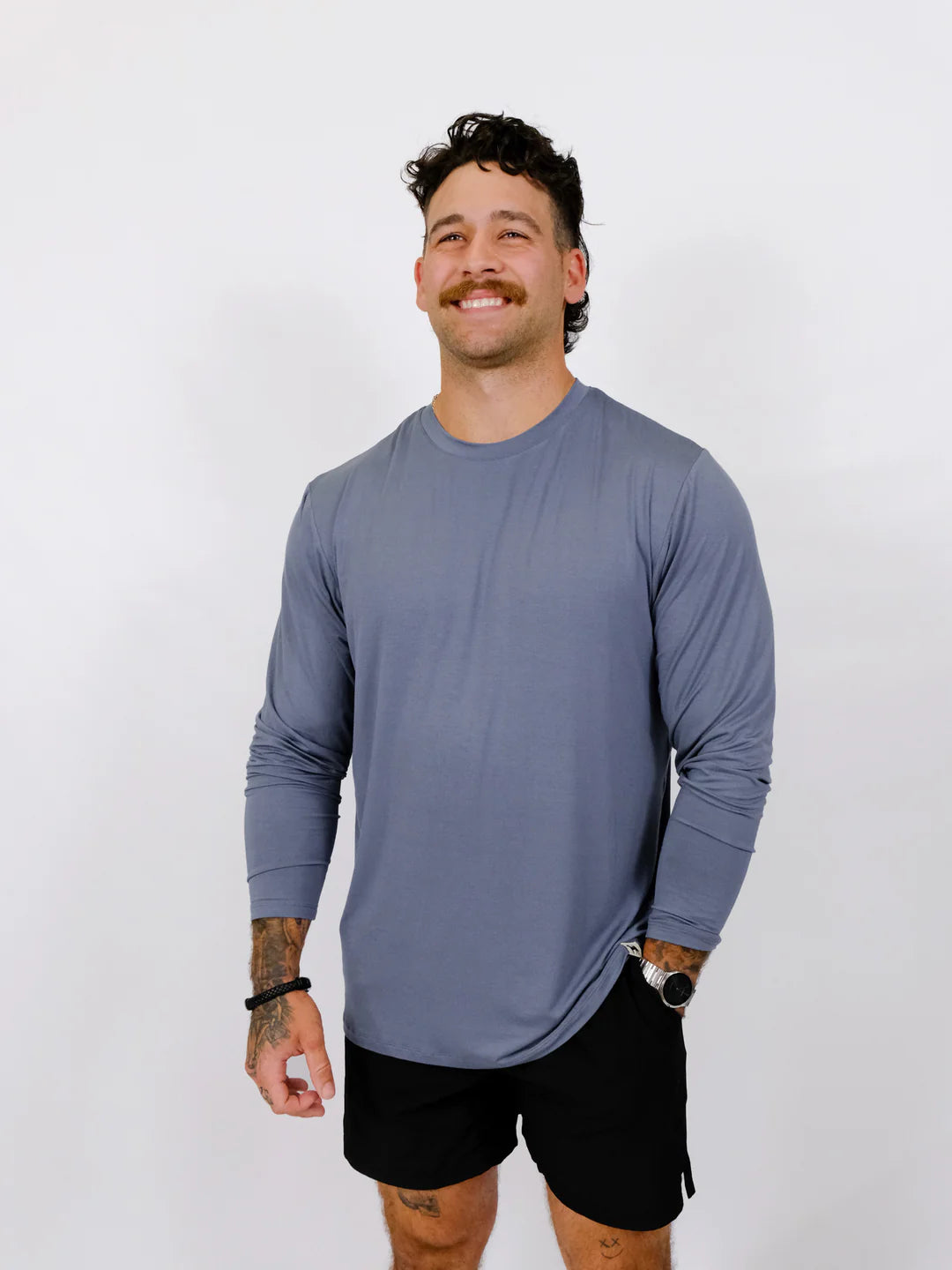 Man wearing a blue long-sleeve shirt and black shorts against a white background