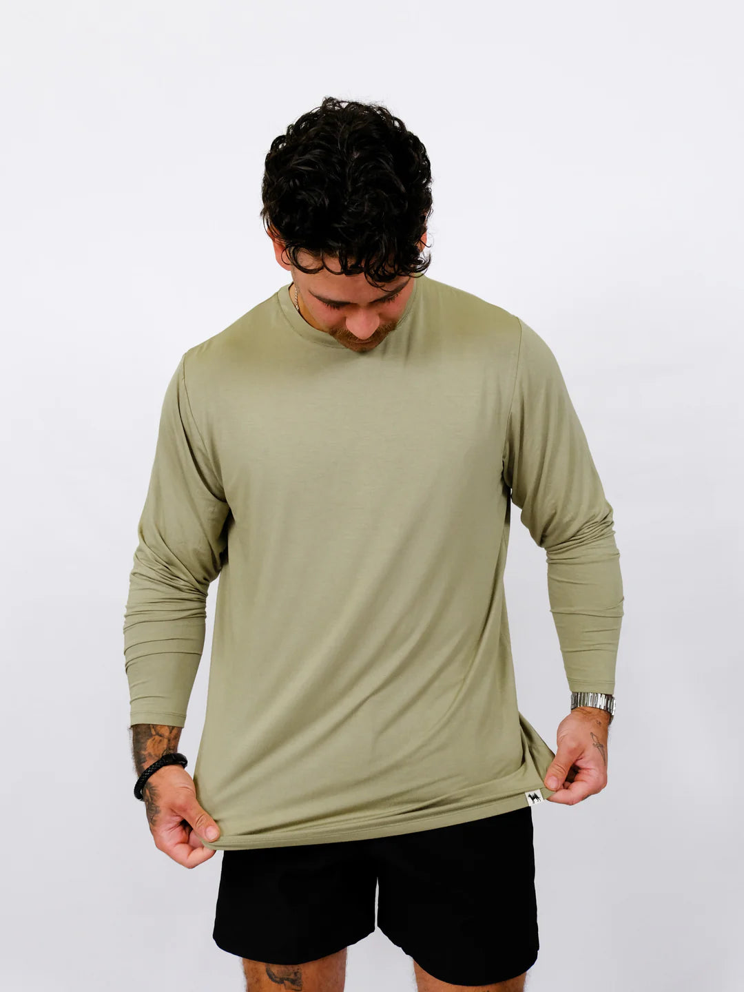 Man wearing a green long-sleeve shirt and black shorts on a white background