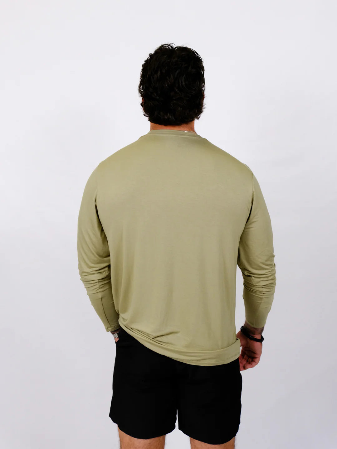 Person wearing a green long-sleeve shirt and black shorts on a white background